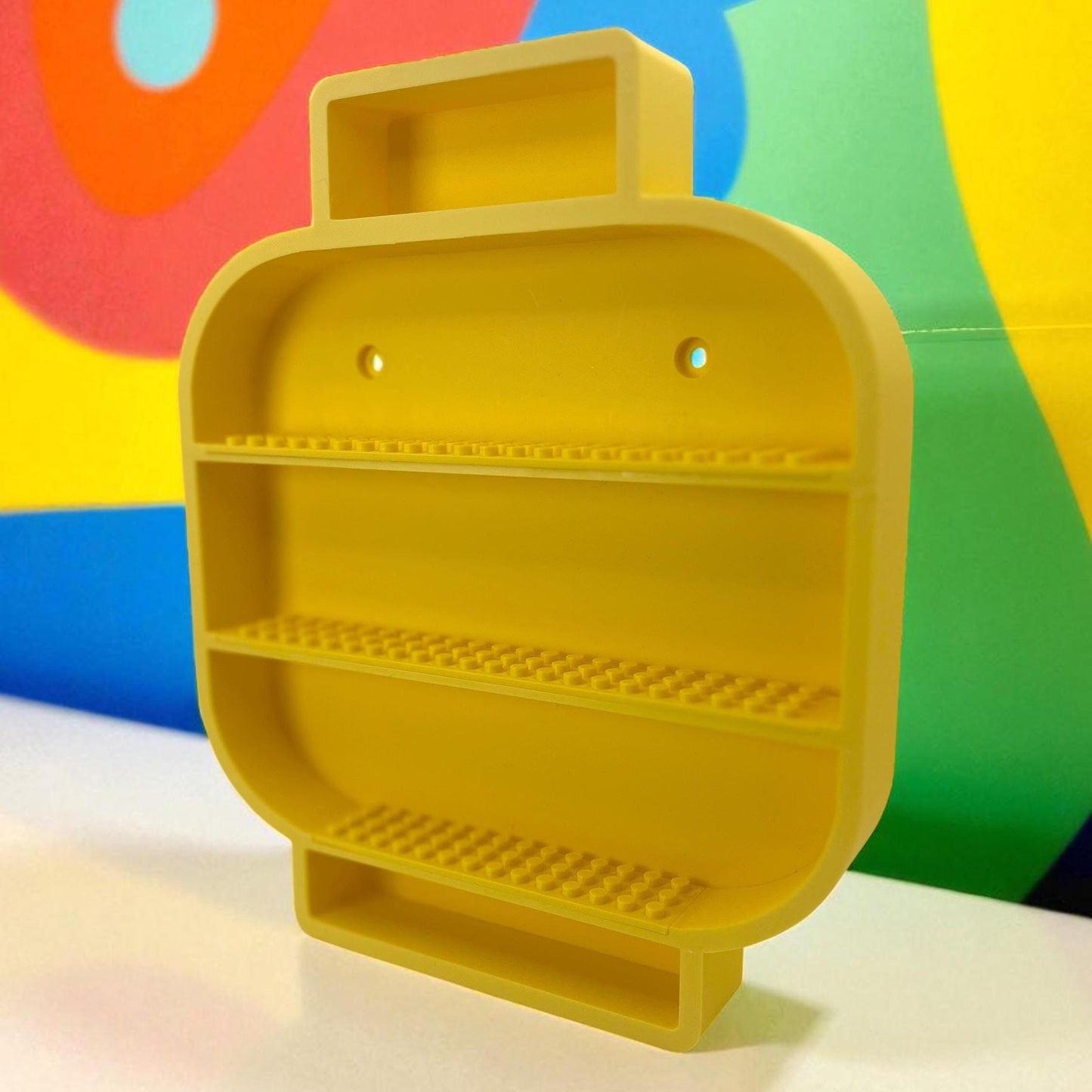 Yellow 3D printed minifigure head shaped shelf with open compartments for displaying small toys or collectibles.